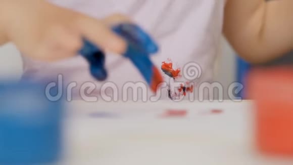 一个穿着彩色衣服的小女孩的特写画在明亮颜色的纸上把他的手指浸在油漆罐里视频的预览图