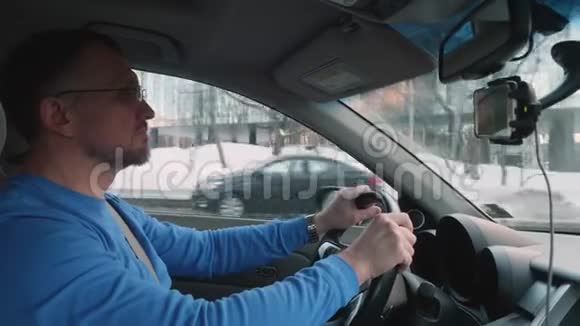 阳光明媚的下午身穿蓝色衬衫戴着眼镜的白人司机在雪城开车侧视图视频的预览图