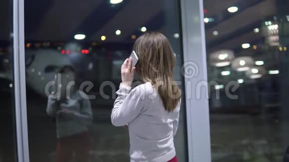 年轻漂亮的女孩在空着的机场候机楼里对着飞机打电话视频的预览图