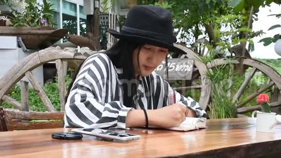 旅行者泰国女人坐在书上写纸条在花园里回忆视频的预览图