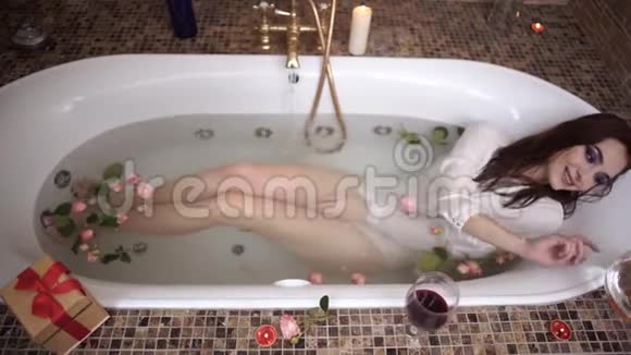 穿着白衬衫妆容亮丽的年轻女子躺在浴缸里捧着玫瑰花水从水龙头流出女孩视频的预览图