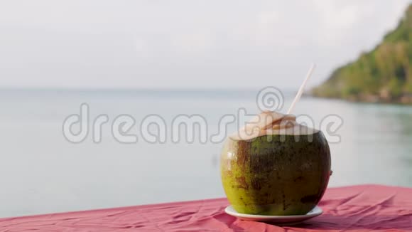 海滩上的一张木桌上放着椰子饮料的视频地平线上有着平静和阳光的海景视频的预览图