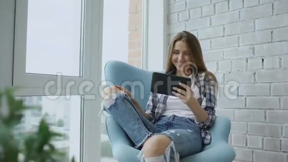 年轻幸福的女人坐在现代阁楼公寓的阳台上用数码平板电脑在线视频聊天视频的预览图