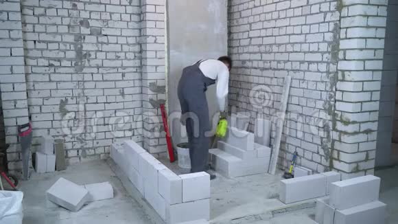 年轻男性建筑工人在铺设前用喷水器湿润砌块视频的预览图