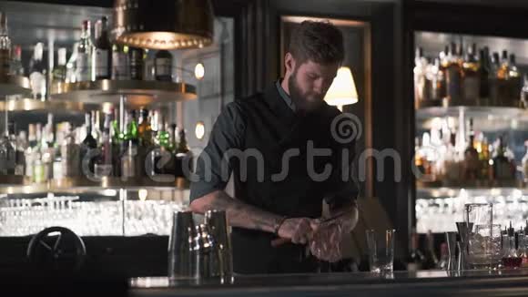 高胡子的酒保拿着刀站在酒吧柜台上压碎了一大块冰在酒吧里做鸡尾酒视频的预览图