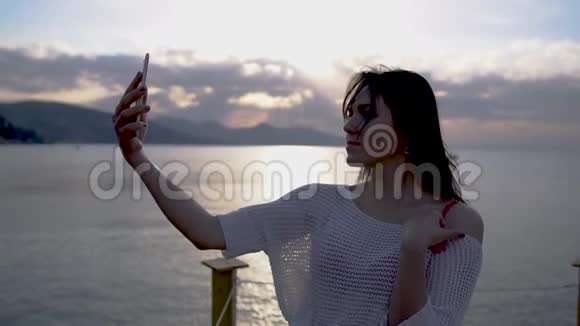 美丽的黑发年轻女子在日出时慢镜头拍摄靠海的自拍照片视频的预览图