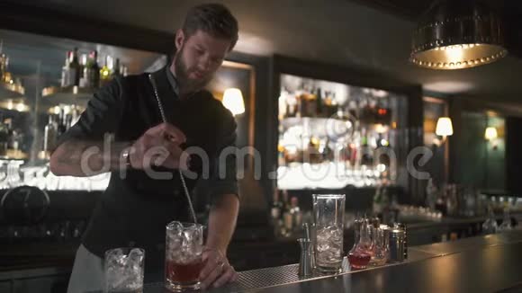漂亮的胡子酒保把朗姆酒和冰块和长金属棒混合在玻璃杯里现代酒吧酒吧的酒吧男招待视频的预览图