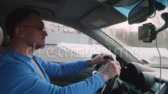阳光明媚的下午身穿蓝色衬衫戴着眼镜的白人司机在雪城开车侧视图视频的预览图