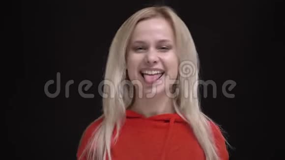 穿着红色毛衣的白毛白种人年轻女孩的肖像在黑色背景下快乐地将滑稽的面孔制成照相机视频的预览图