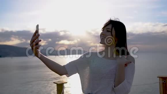美丽的黑发年轻女子在日出时慢镜头拍摄靠海的自拍照片视频的预览图
