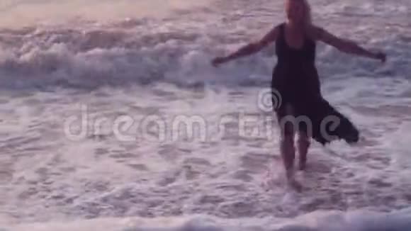 穿着黑色裙子的女人跑到她身边张开双臂拥抱大海上的巨浪视频的预览图