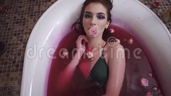 一幅年轻女子的画像她嘴里捧着玫瑰躺在浴缸里喝着红酒女士在看视频的预览图