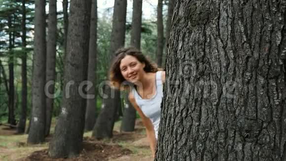 一个女孩从树后面往外看向她招手视频的预览图