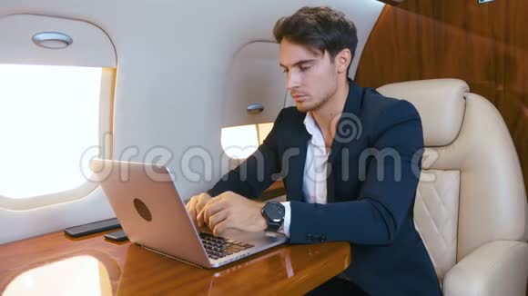 年轻的商人在私人飞机上用笔记本电脑工作成功的商业百万人头等舱旅行视频的预览图