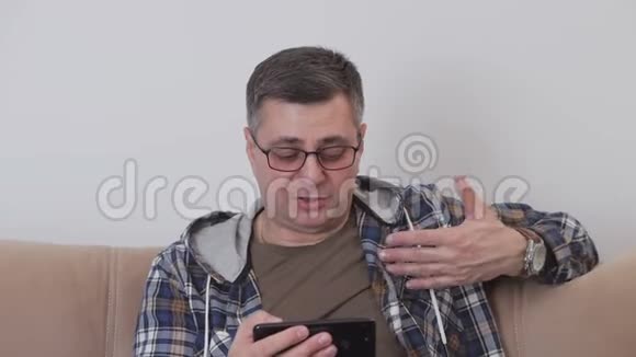一个中年男人坐在沙发上用智能手机里的视频通话与另一个人交流视频的预览图