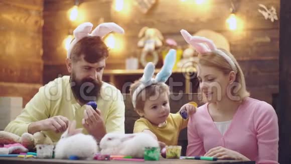 小男孩和他的父母一起为复活节画彩色鸡蛋家庭粉刷复活节彩蛋幸福的家庭正在准备视频的预览图