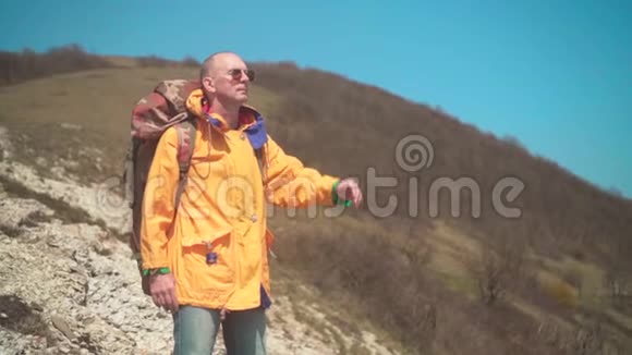 一个穿着黄色夹克眼镜和一个大型旅游背包的人站在山上视频的预览图