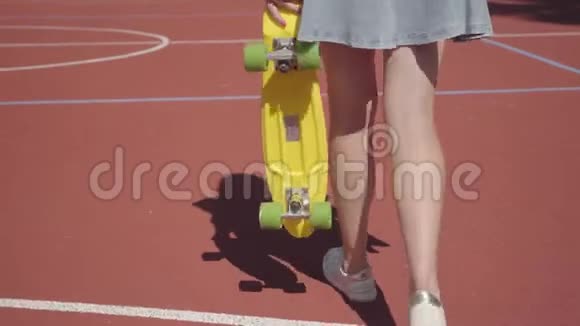 腿的女人穿着短裙带着黄色滑板在篮球场上行走穿运动鞋的女人腿视频的预览图