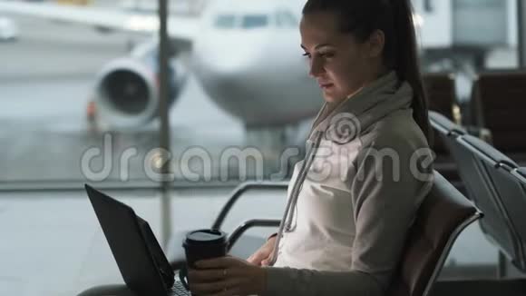 女自由职业者一边看一边喝外卖咖啡一边用笔记本电脑在机场候机室工作视频的预览图