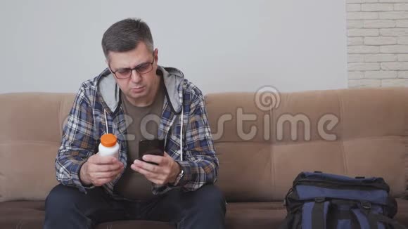 一个人坐在沙发上手里拿着一罐药丸用手机附近有一个大型旅游背包视频的预览图