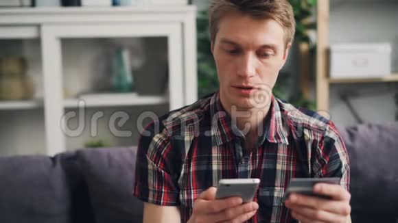 开朗的年轻人正在用银行卡在线支付触摸智能手机屏幕然后快乐地微笑财务视频的预览图