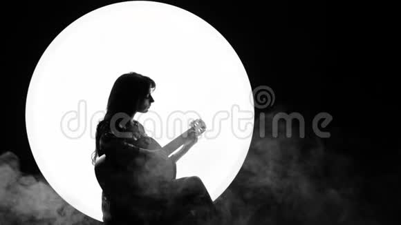 女音乐家的剪影一个年轻的女人坐在白色圆圈背景上弹着一把吉他就像满月一样视频的预览图