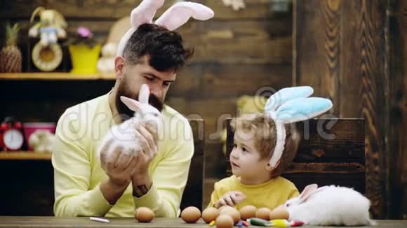 有兔子耳朵的男孩看着毛茸茸的小兔子男人抱着复活节兔子幸福的家庭正在准备复活节视频的预览图