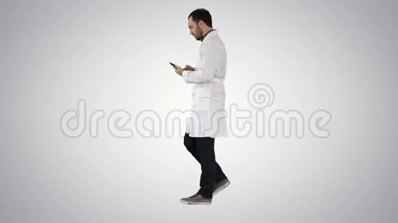 男性医生在梯度背景下行走和使用手机视频的预览图