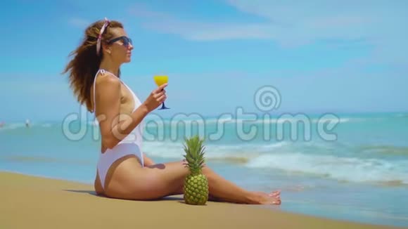 快乐美丽的小女孩坐在海边的沙滩上拿着菠萝和果汁视频的预览图