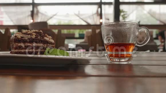 用透明杯子从玻璃茶壶里倒热茶夏季咖啡厅木制桌子上的茶杯和巧克力派视频的预览图