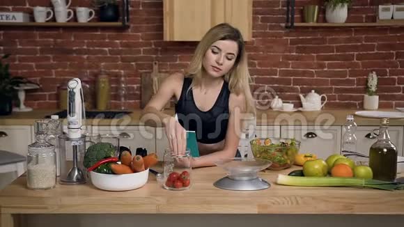 年轻的女运动员正在给樱桃西红柿称重准备健康食品并在厨房的笔记本上记录食谱视频的预览图