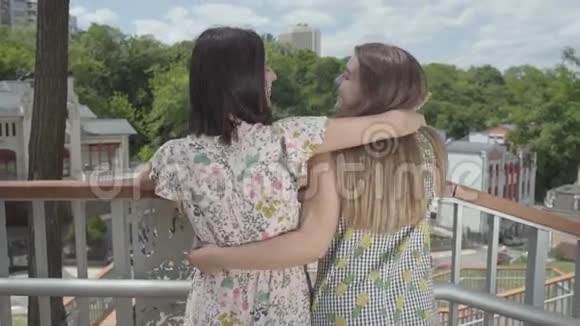 两个迷人的女孩站在户外拥抱和交谈欣赏美丽的城市景观女朋友的谈话视频的预览图