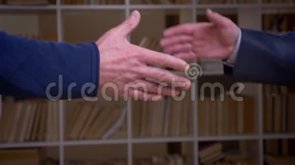 特写镜头两位老商业伙伴握手的书架背景视频的预览图