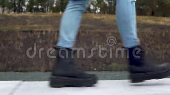 一个女人穿着黑色的大靴子沿着混凝土栅栏走特写视频的预览图