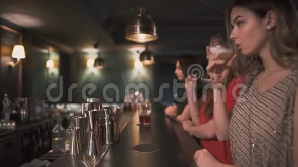 三个心烦意乱和愤怒的年轻女孩坐在酒吧旁一个接一个地喝鸡尾酒试图忘记和喝醉视频的预览图