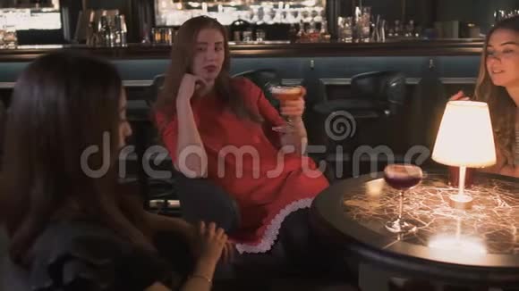三个穿着漂亮的年轻女孩坐在靠近舒适桌子的酒吧旁喝着鸡尾酒聊着生活视频的预览图