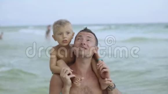 年轻的父亲和他的小儿子在海滩上玩得很开心儿子坐在爸爸肩膀上视频的预览图