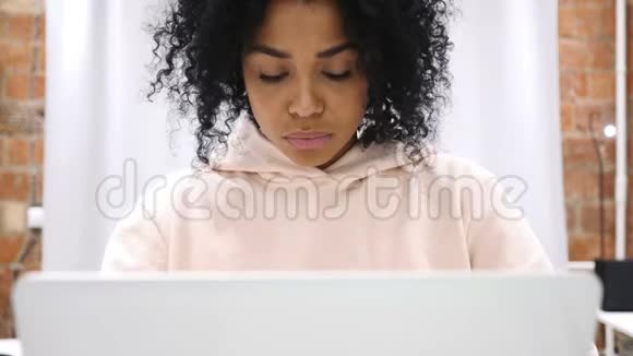 兴奋的非裔美国妇女在笔记本电脑上坐在沙发上庆祝成功视频的预览图