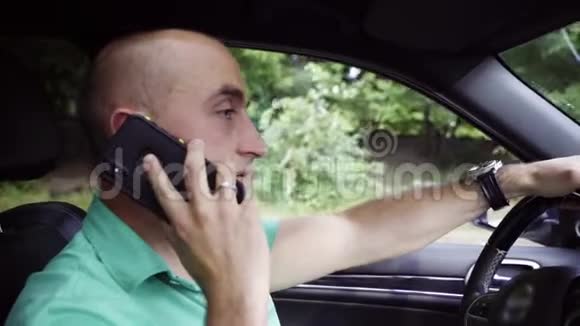 穿绿色t恤的漂亮秃头在智能手机驾驶汽车上讲话视频的预览图