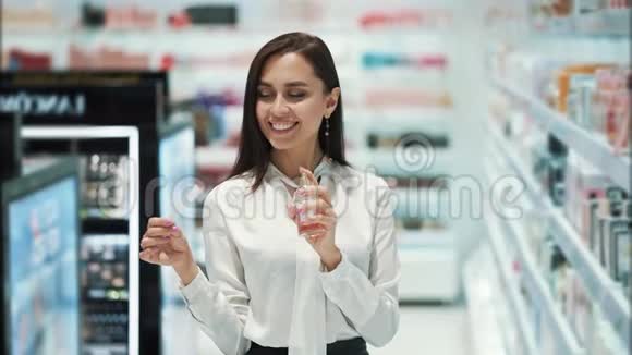 漂亮的女孩在化妆品店里选择香水喷在测试器上嗅嗅视频的预览图