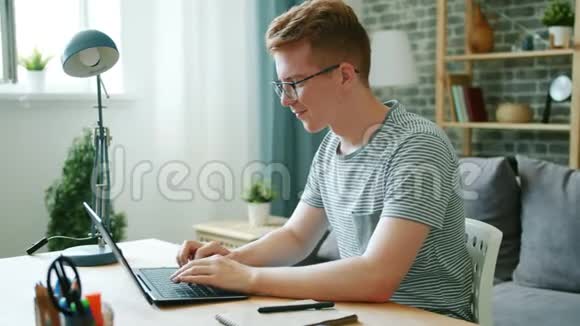 青少年自由职业者在家拿着笔记本电脑在办公桌前微笑打字视频的预览图