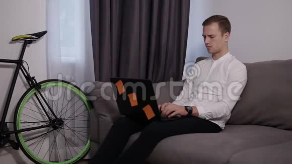 年轻迷人的男人坐在沙发上在家里上网工作使用互联网空闲时间放松现代视频的预览图