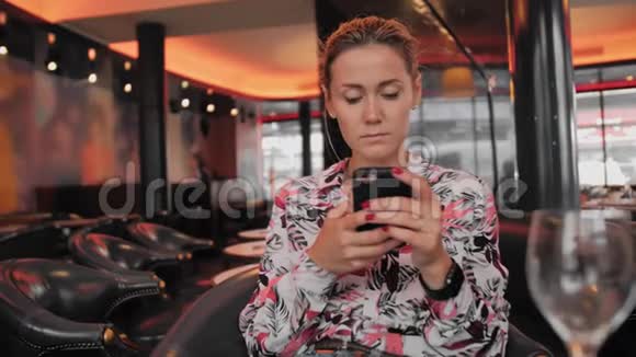 年轻的法国女性使用社交网络与手机通信坐在皮椅上的餐厅里视频的预览图