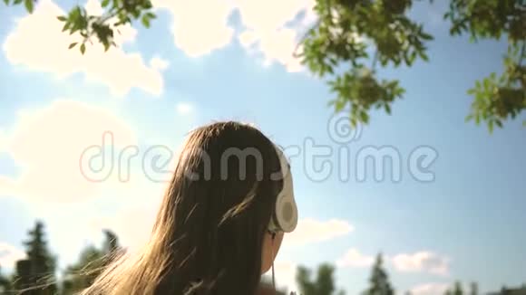 一个女孩带着耳机走在城市街道上在蓝天下听音乐慢动作女孩在旅行视频的预览图