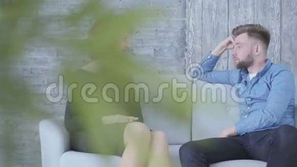 写真相当优雅的成熟女子与身穿蓝色衬衫的年轻男子近距离坐在家里的沙发上聊天植物视频的预览图