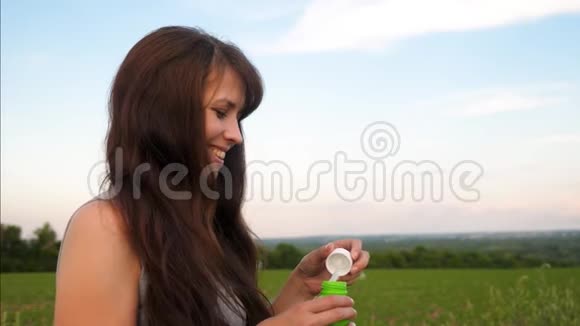 快乐的长发女孩在蓝天上吹出透明的肥皂泡微笑着慢动作视频的预览图