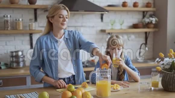 妈妈和女儿在厨房里做天然橙汁迷人的年轻妈妈把橙汁挤成一团视频的预览图
