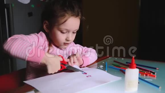 可爱的小学龄前欧洲女孩穿着粉红色毛衣把她的画从纸上剪下来和别人说话视频的预览图