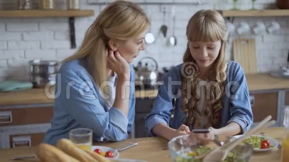 10岁的女孩在社交网络上展示妈妈的帖子妈妈和女儿在午餐时用智能手机看东西然后视频的预览图