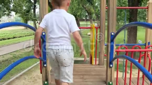 镜头跟随幼儿滑下幼儿游戏区一个快乐的小男孩在孩子们公园里玩耍视频的预览图